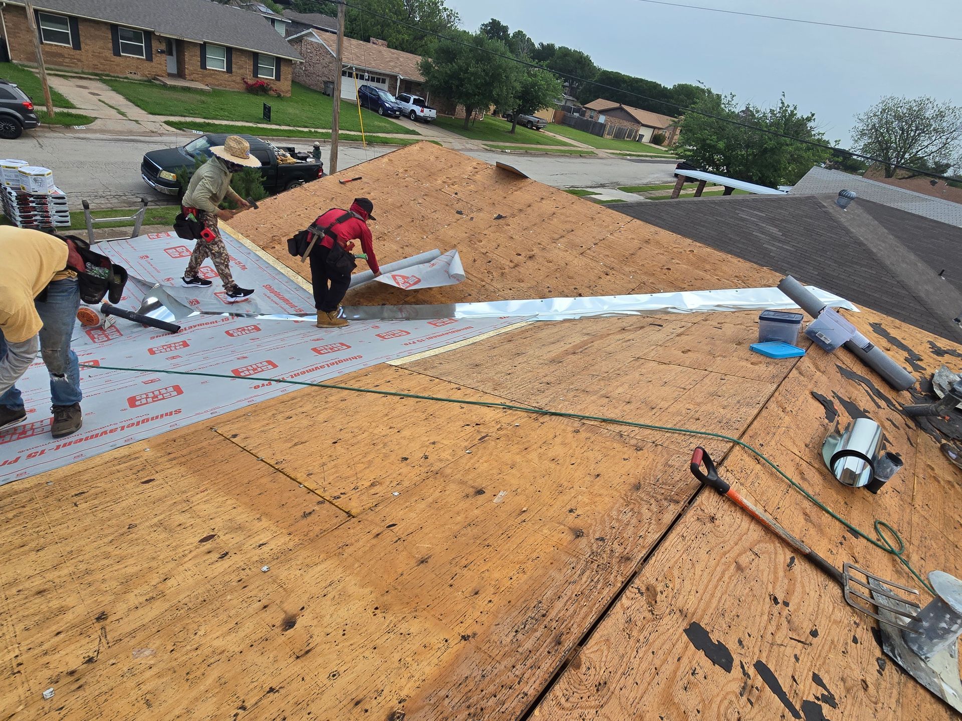 Workers installing roofing on a house, with underlayment and tools on a steep roof.
