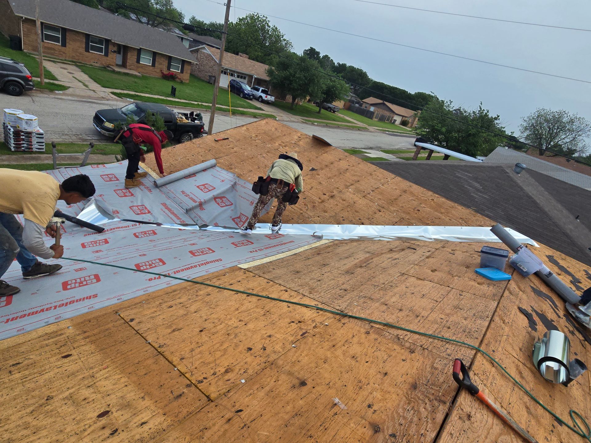 Workers installing roofing underlayment on a sloped roof at a residential construction site