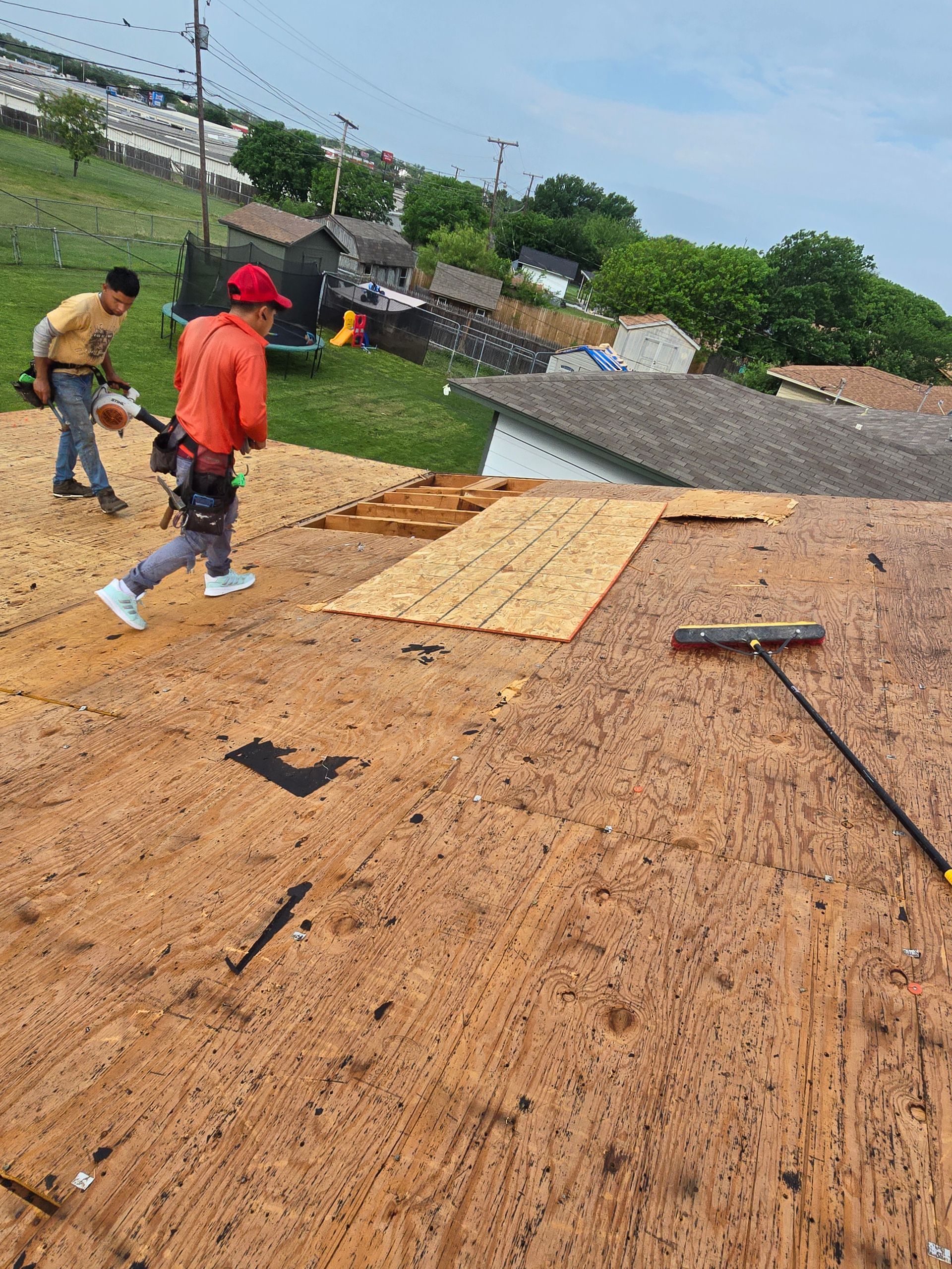 Workers repairing a roof with plywood sheets and tools on a sloped surface.