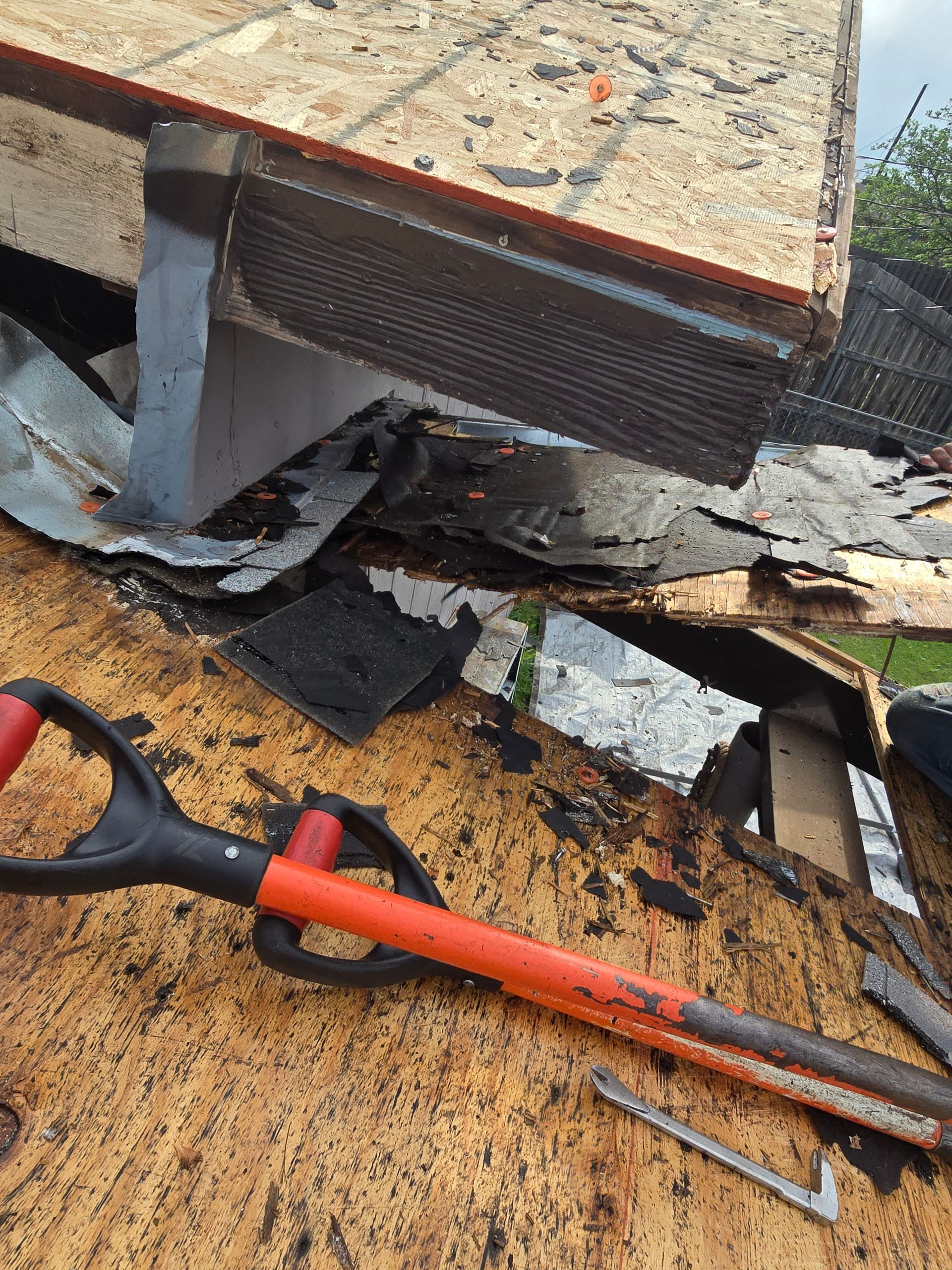 Roof repair tools on a damaged roof, with shingles torn up and a trowel beside a red-handled tool.