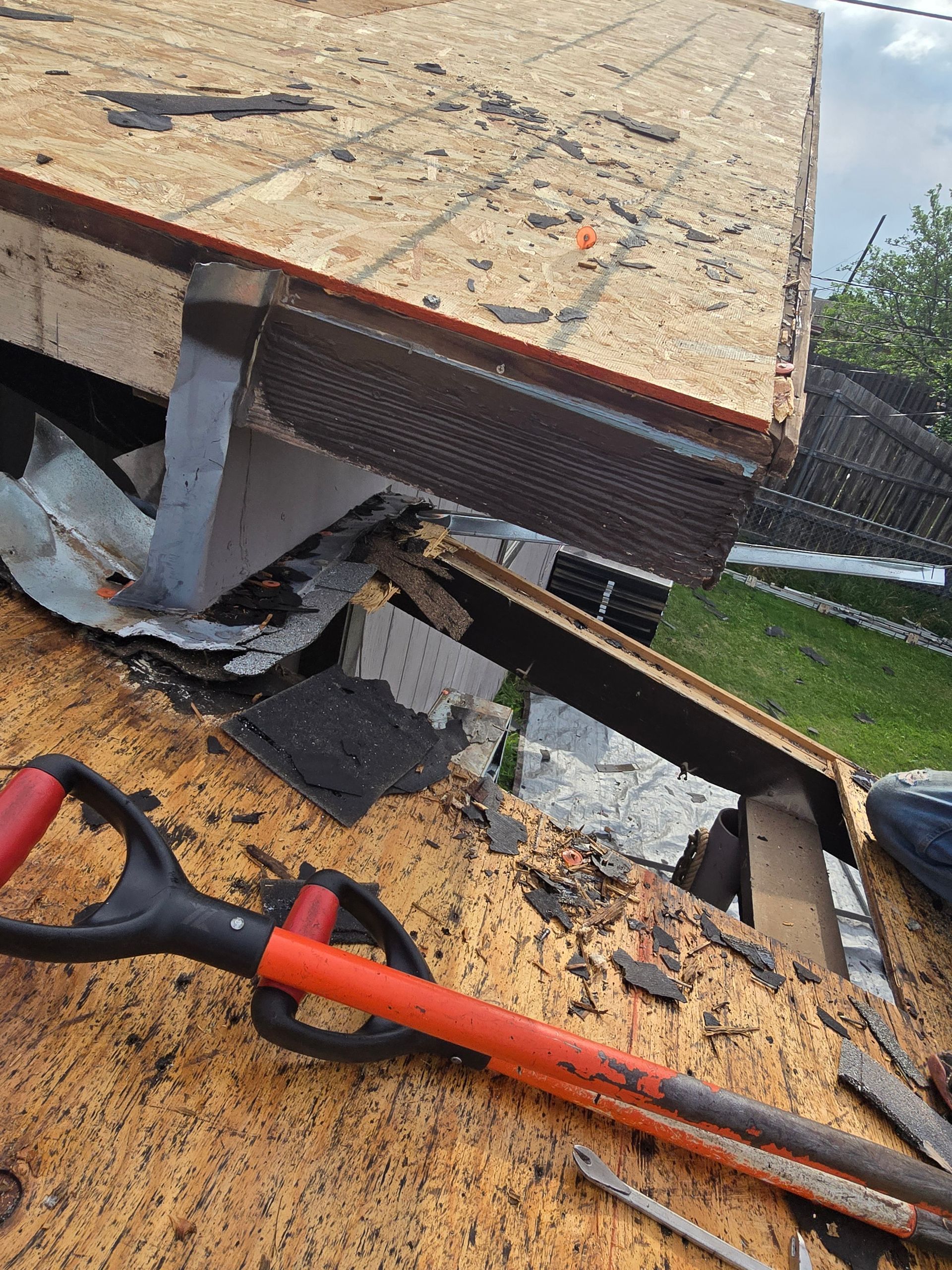 Collapsed roof debris with exposed insulation and orange tools on a slanted surface outdoors