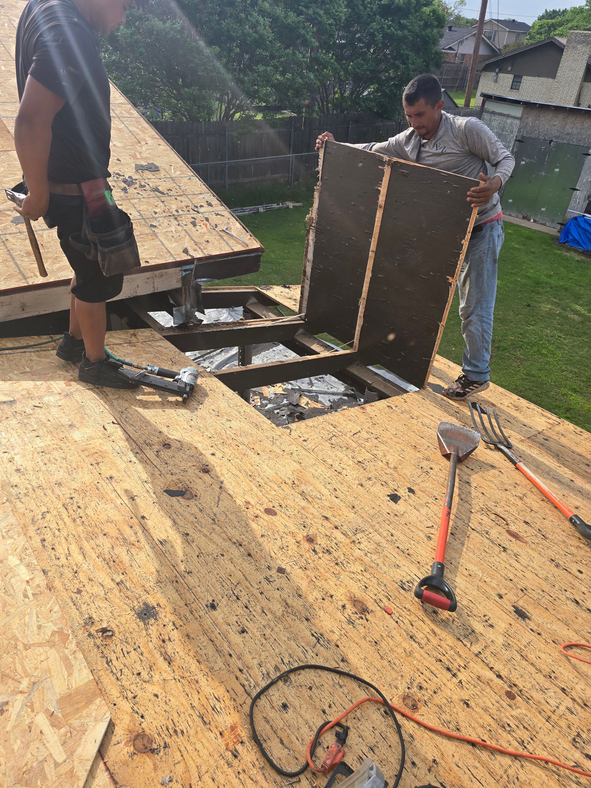 Two workers on a roof installing a hatch frame near tools and exposed roofing materials
