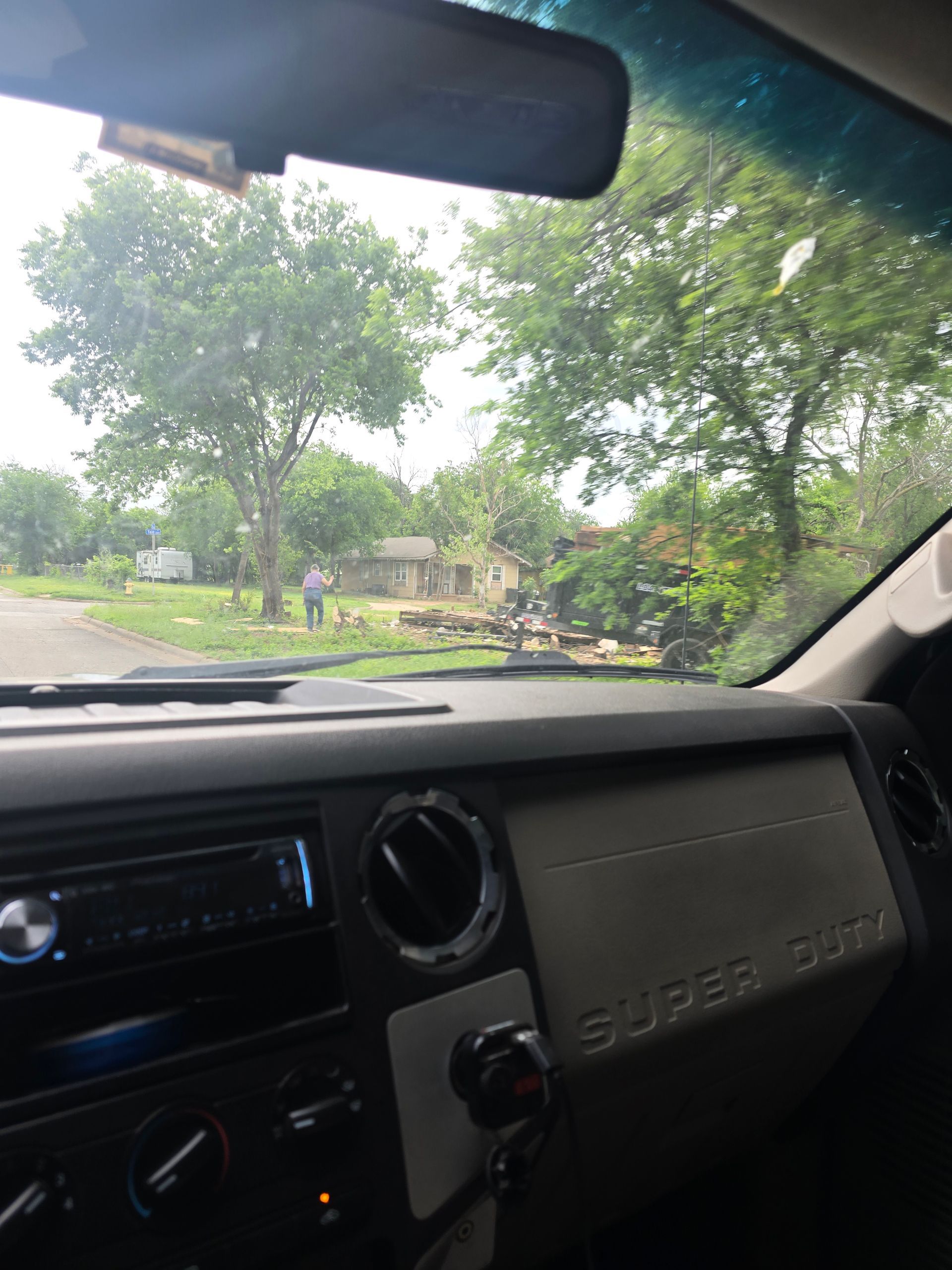View from inside a car through the windshield toward a tree-lined road and parked vehicles.