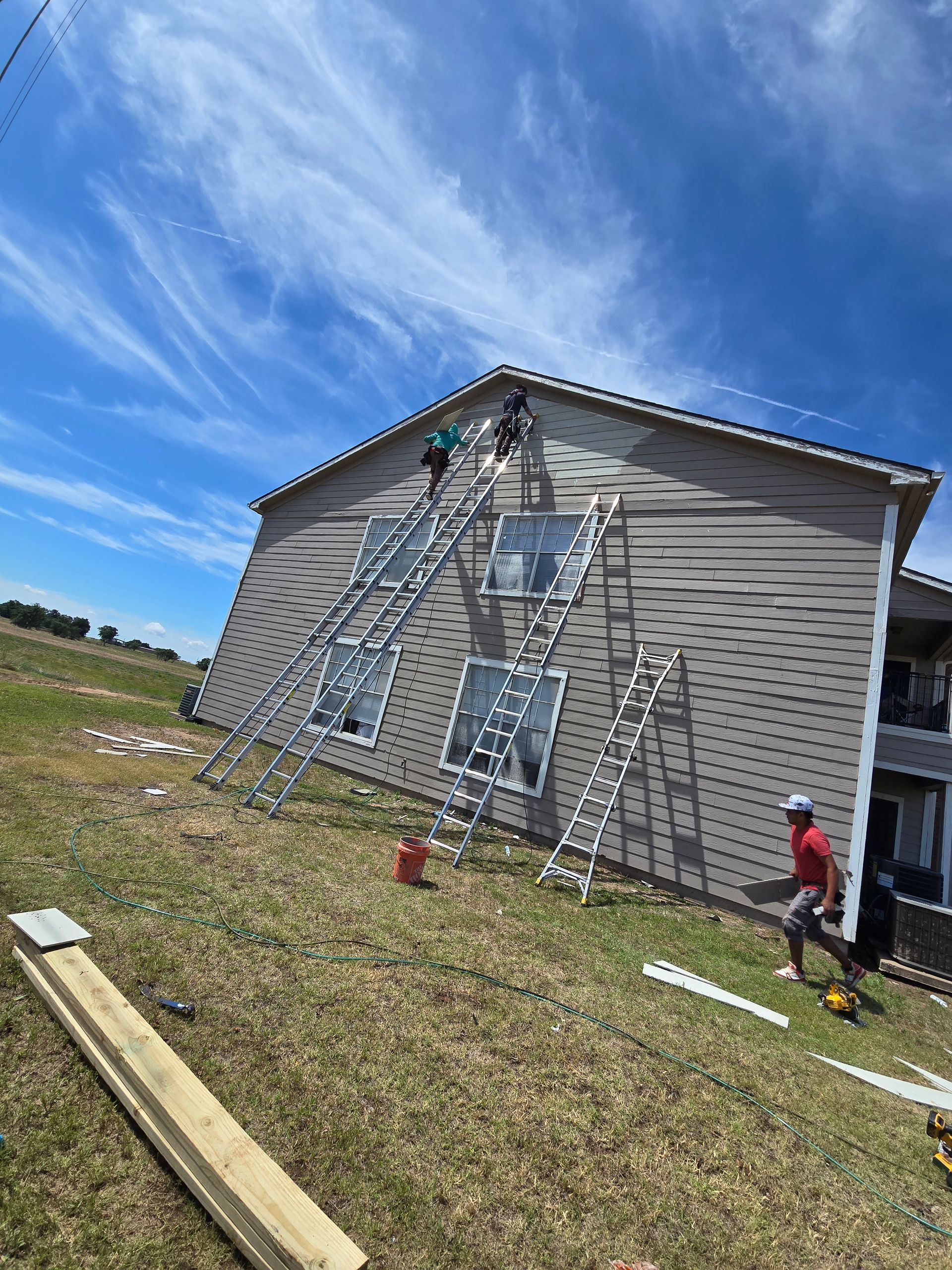 Two workers on ladders painting a house exterior under a blue sky.