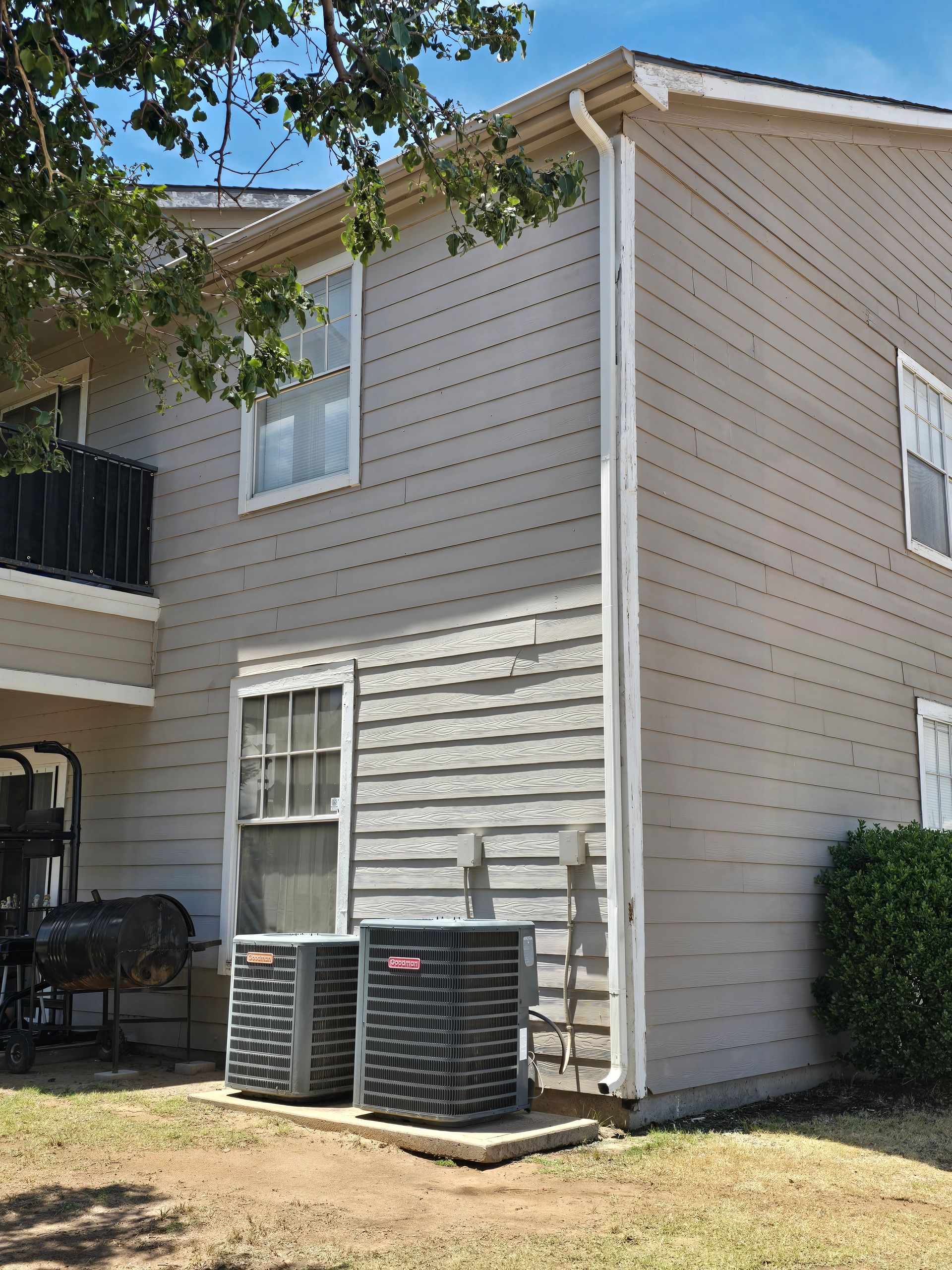 Two-story beige apartment exterior with window AC units and ivy near the roofline