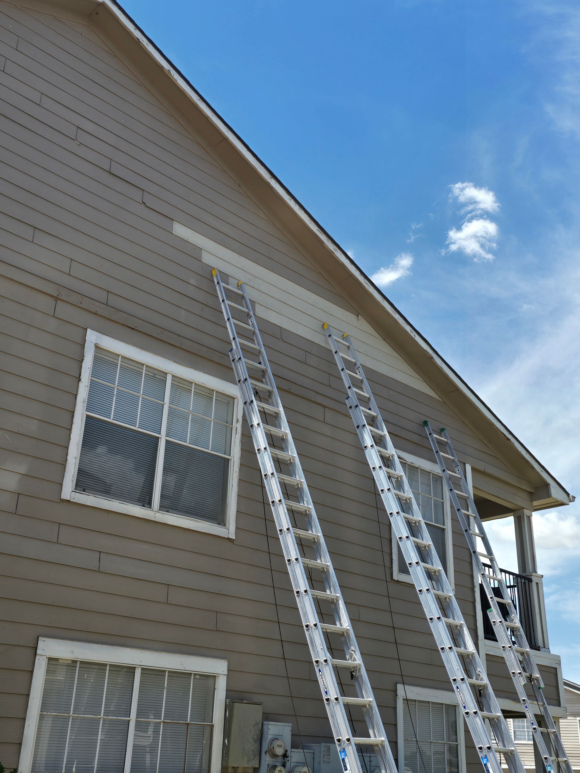 Ladders leaning against a tan house exterior under a blue sky.