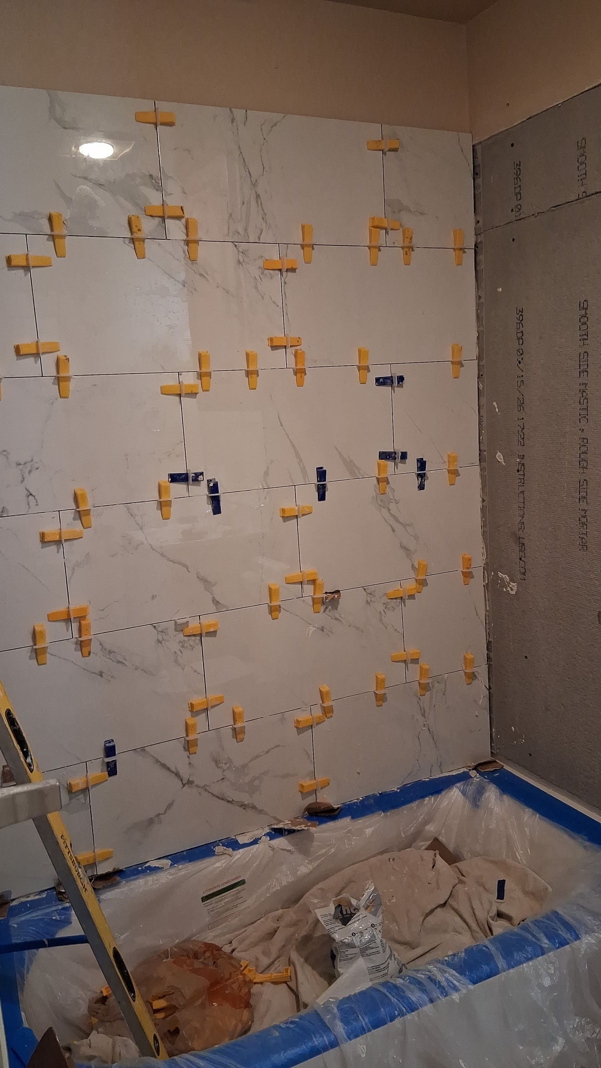 Partially tiled bathroom wall with spacers and blue tape around a shower base under renovation
