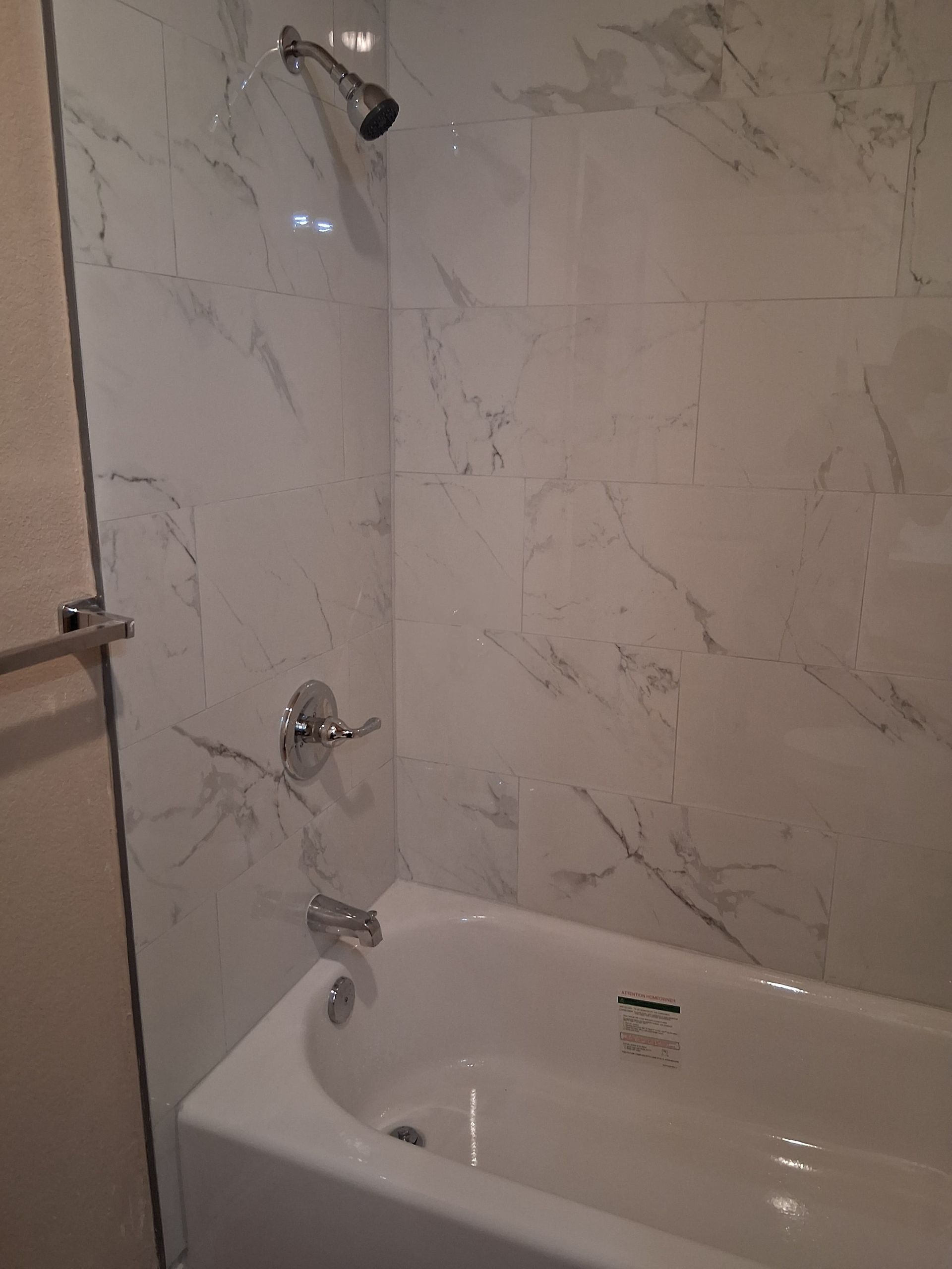 Bathroom shower with white marble tile, chrome fixtures, and a white tub.