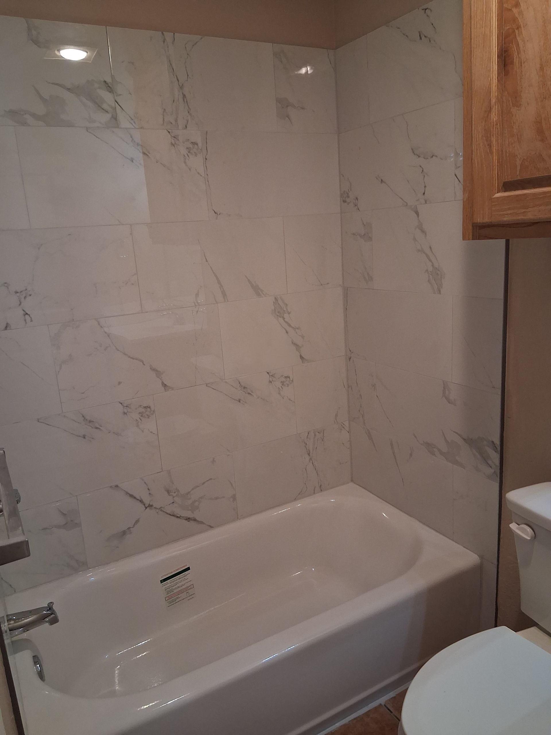 Bathroom with a white bathtub and marble-look wall tiles next to a toilet.