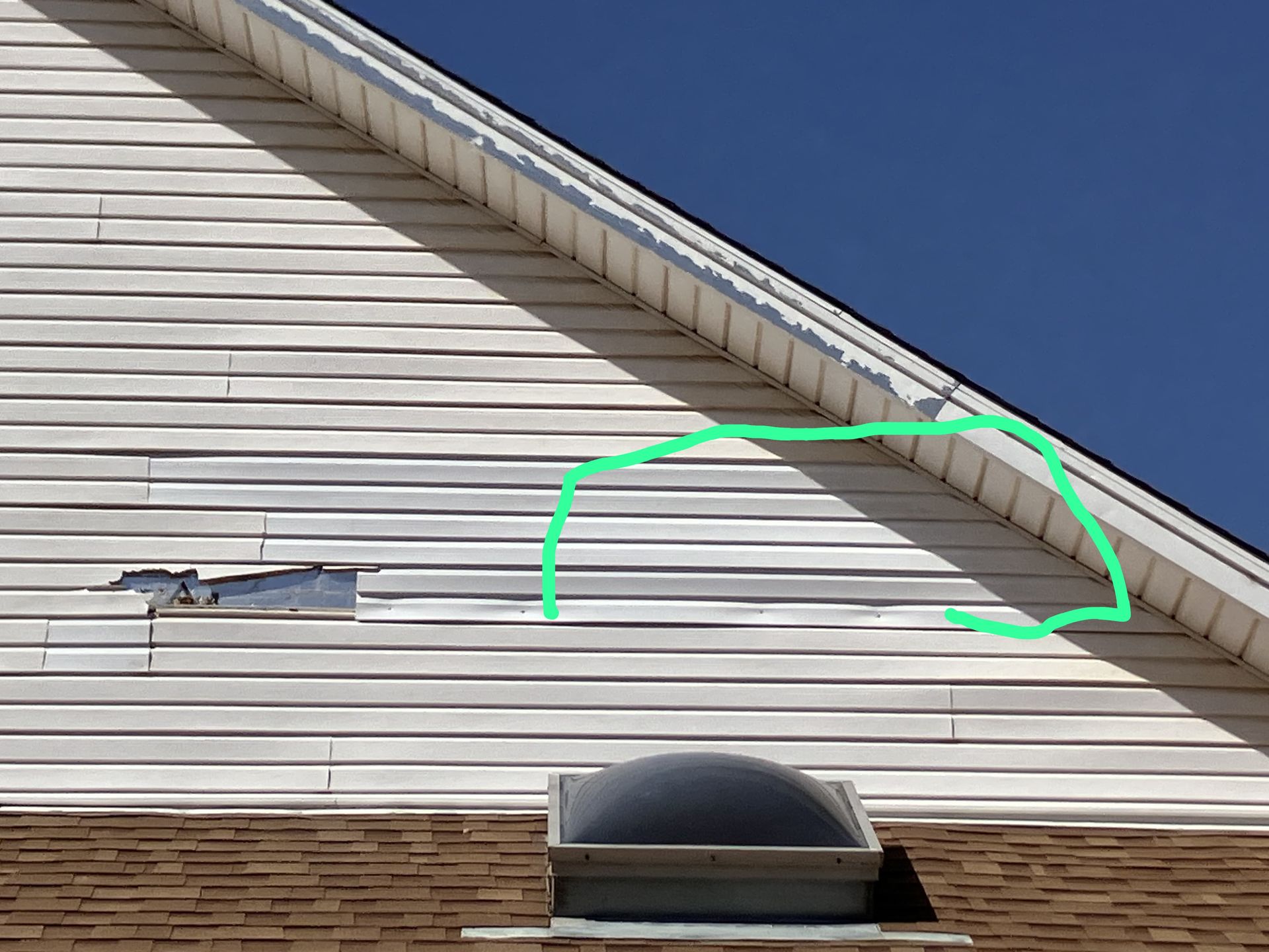 Side of a house with white siding and a green-marked damaged area near the roofline.