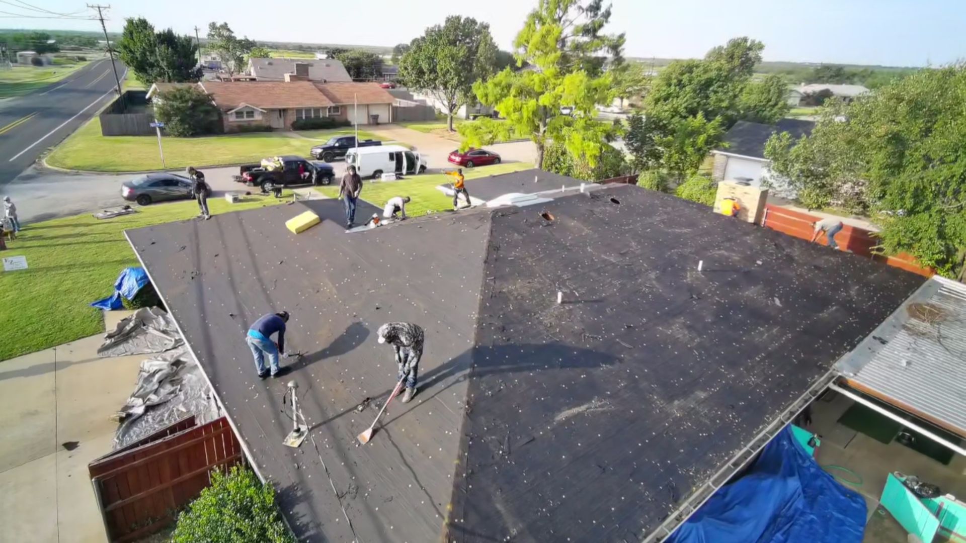 Workers repairing a large black roof with tools and materials on a suburban house.