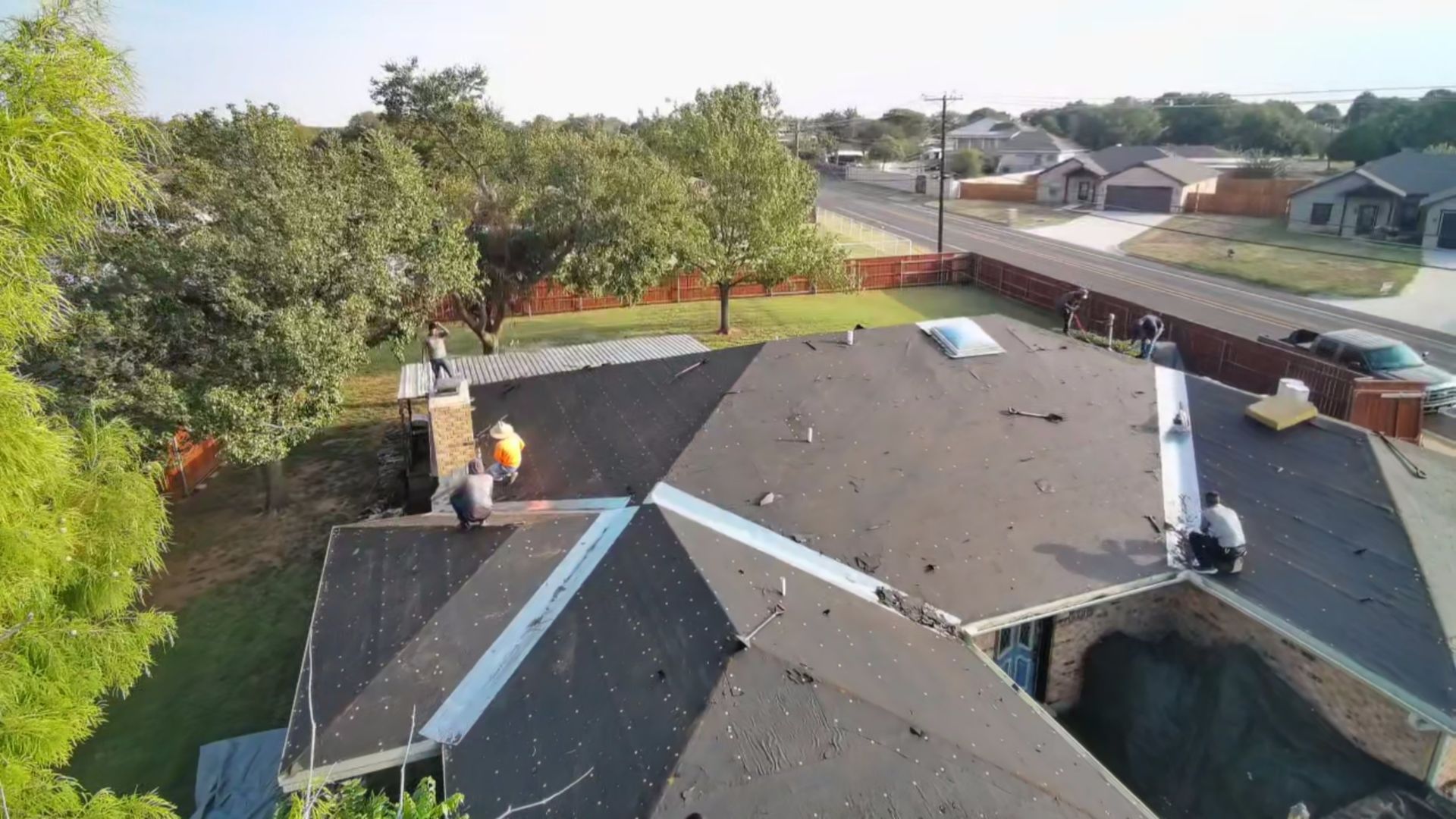 Roofers repairing a shingled suburban house roof, with tools and safety harnesses visible