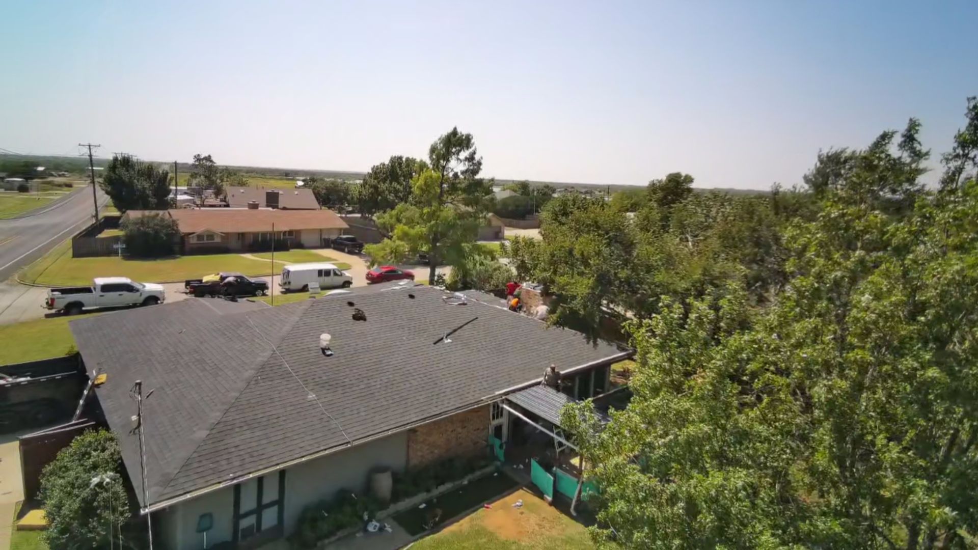 Aerial view of suburban houses, parked cars, and trees under a clear blue sky