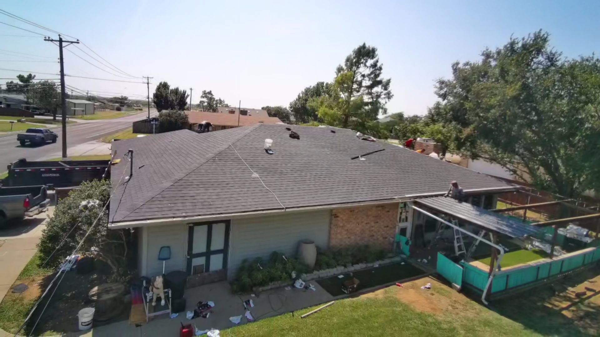 Aerial view of a house with a gray roof, backyard patio, and trees in a suburban neighborhood