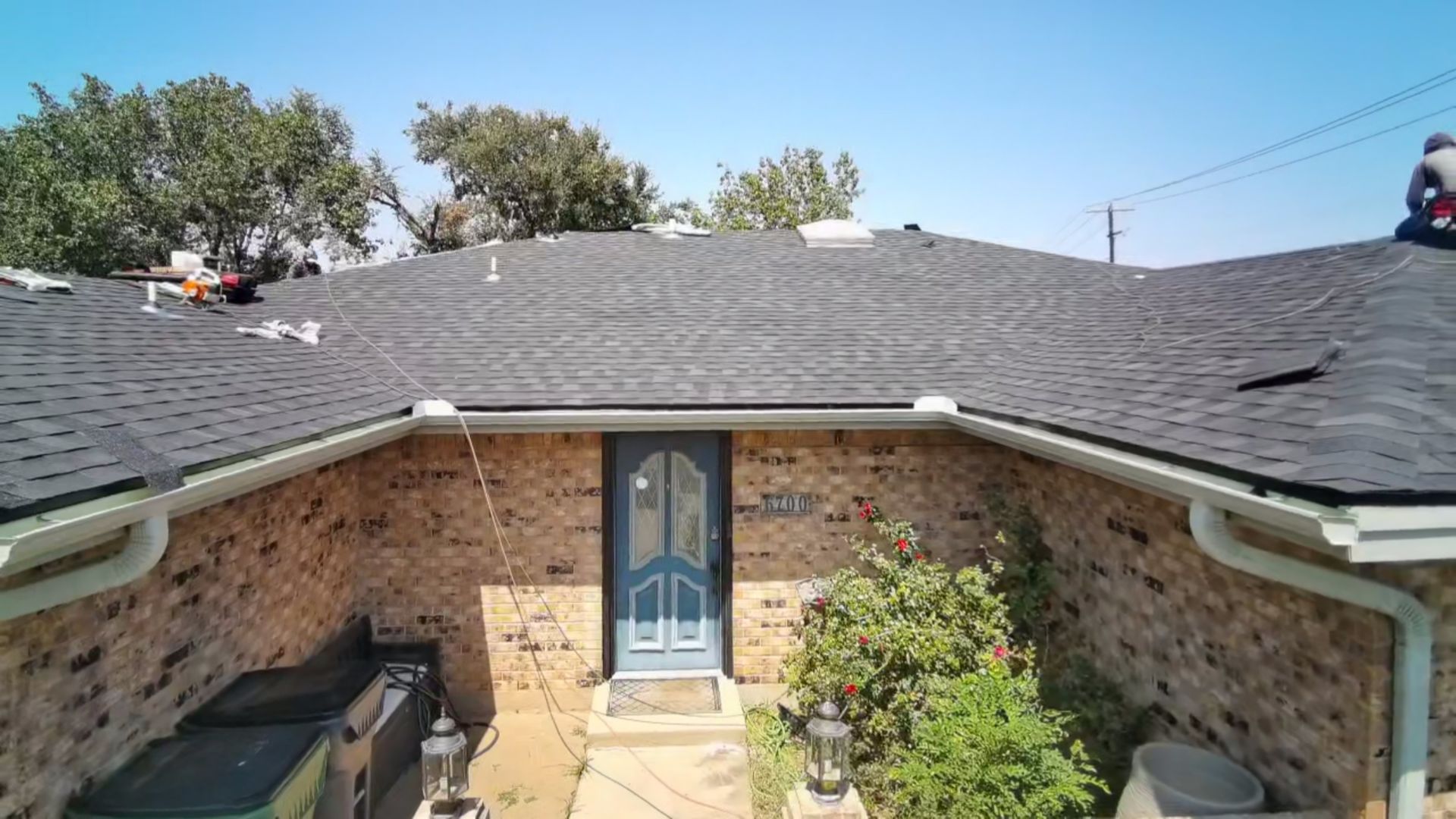 Brick house courtyard with dark shingled roof and blue front door under bright sky
