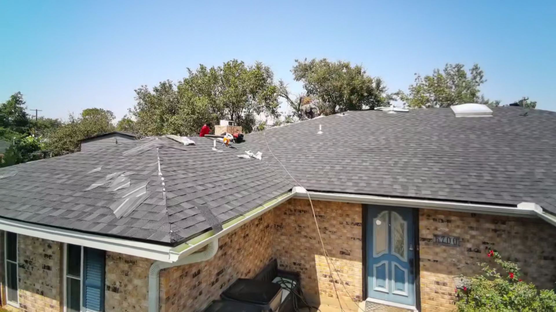 Roofers working on a gray shingle roof above a brick house