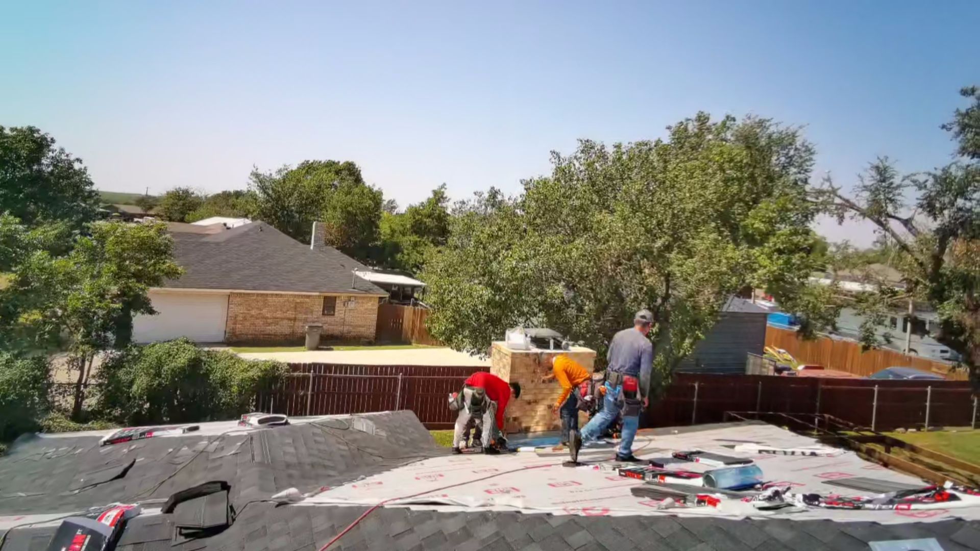 Workers on a roof installing materials near a house on a sunny day.