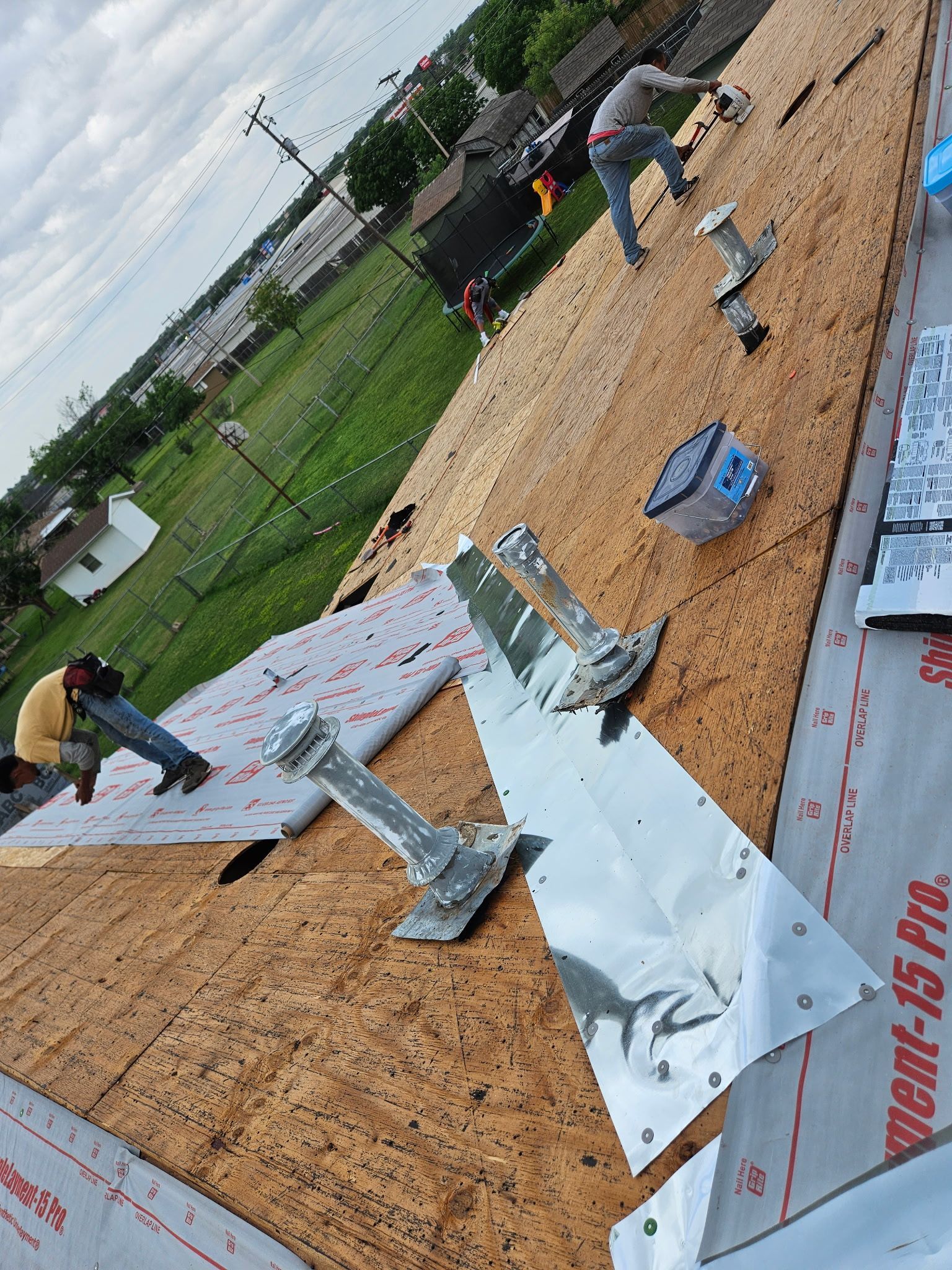 Workers installing roofing underlayment on a sloped roof with white panels and tools nearby