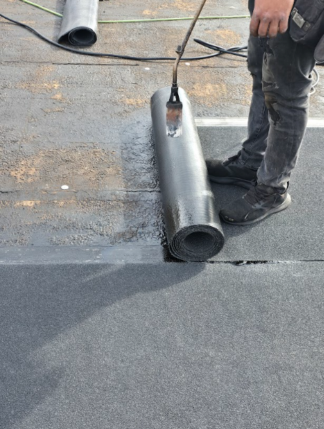 Worker rolling black roofing material on a flat roof