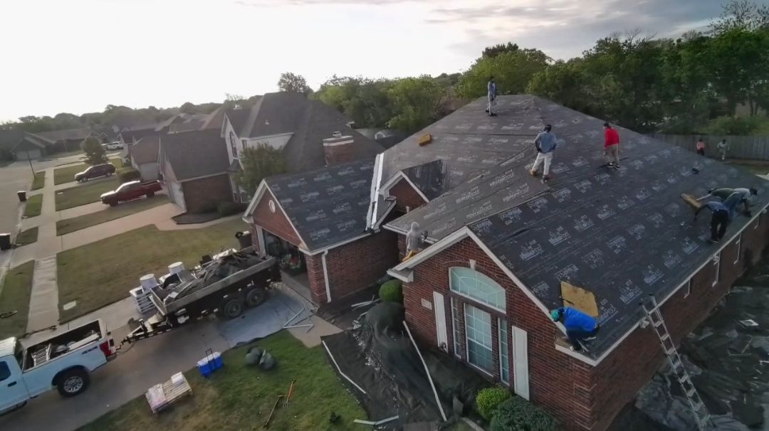 Aerial view of workers on a brick house roof, with tools and materials, in a suburban neighborhood