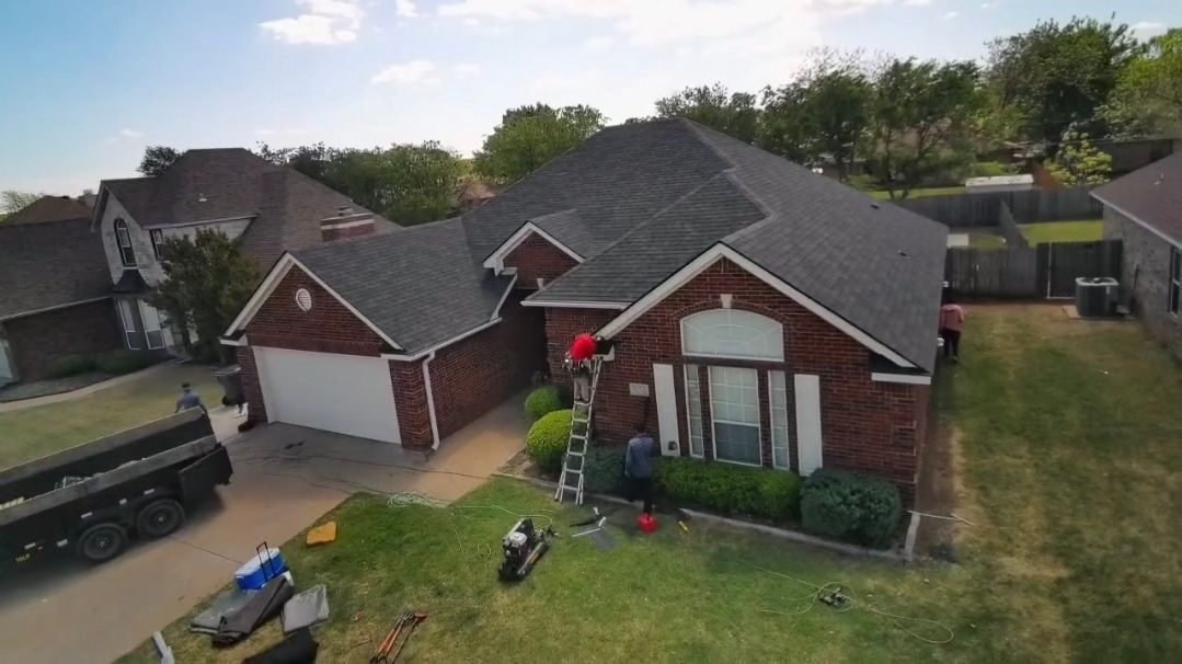 Suburban house with a roof being repaired, workers on a ladder and roof, and tools in the front yard