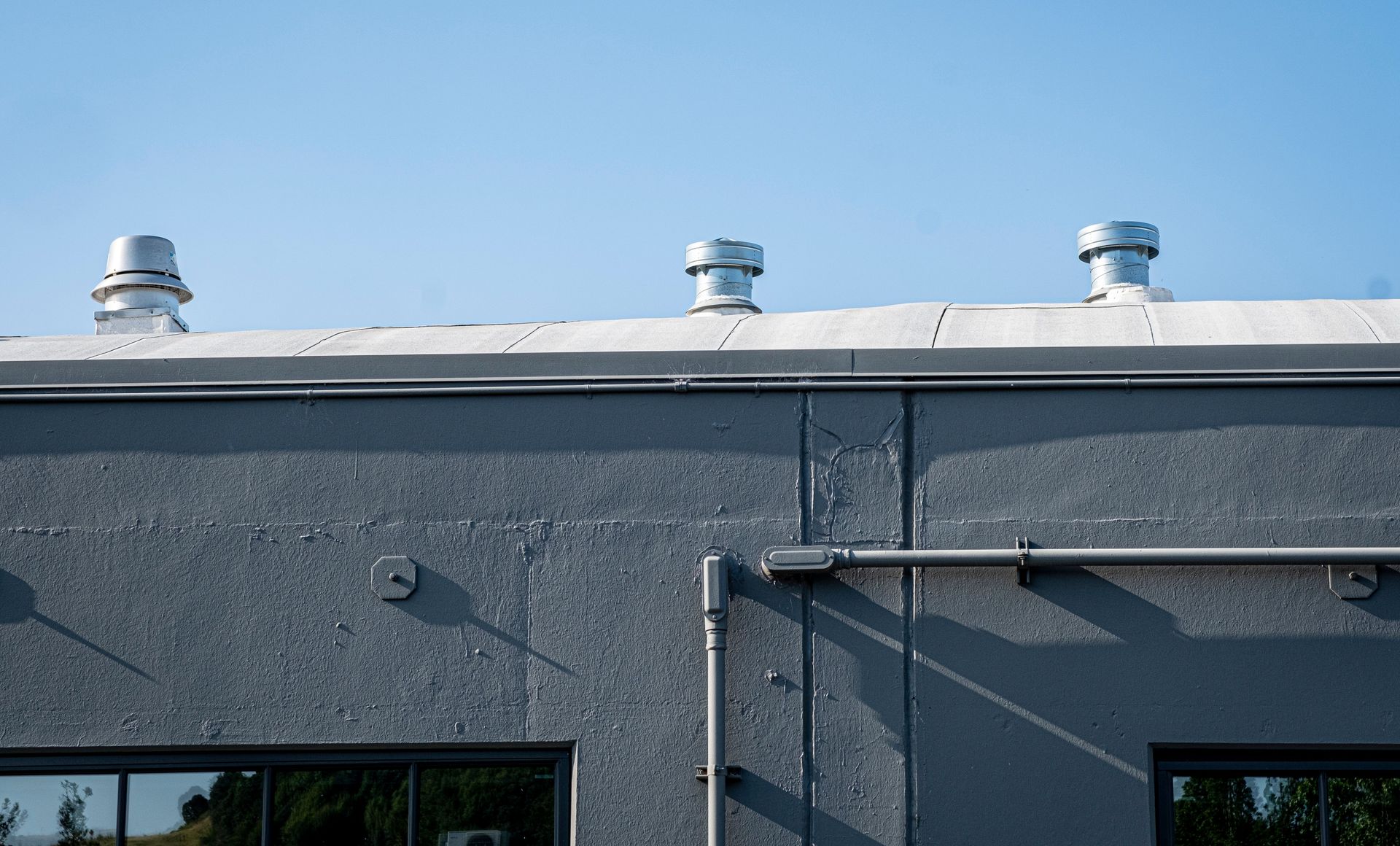 Gray industrial building roof with three silver vents against a blue sky