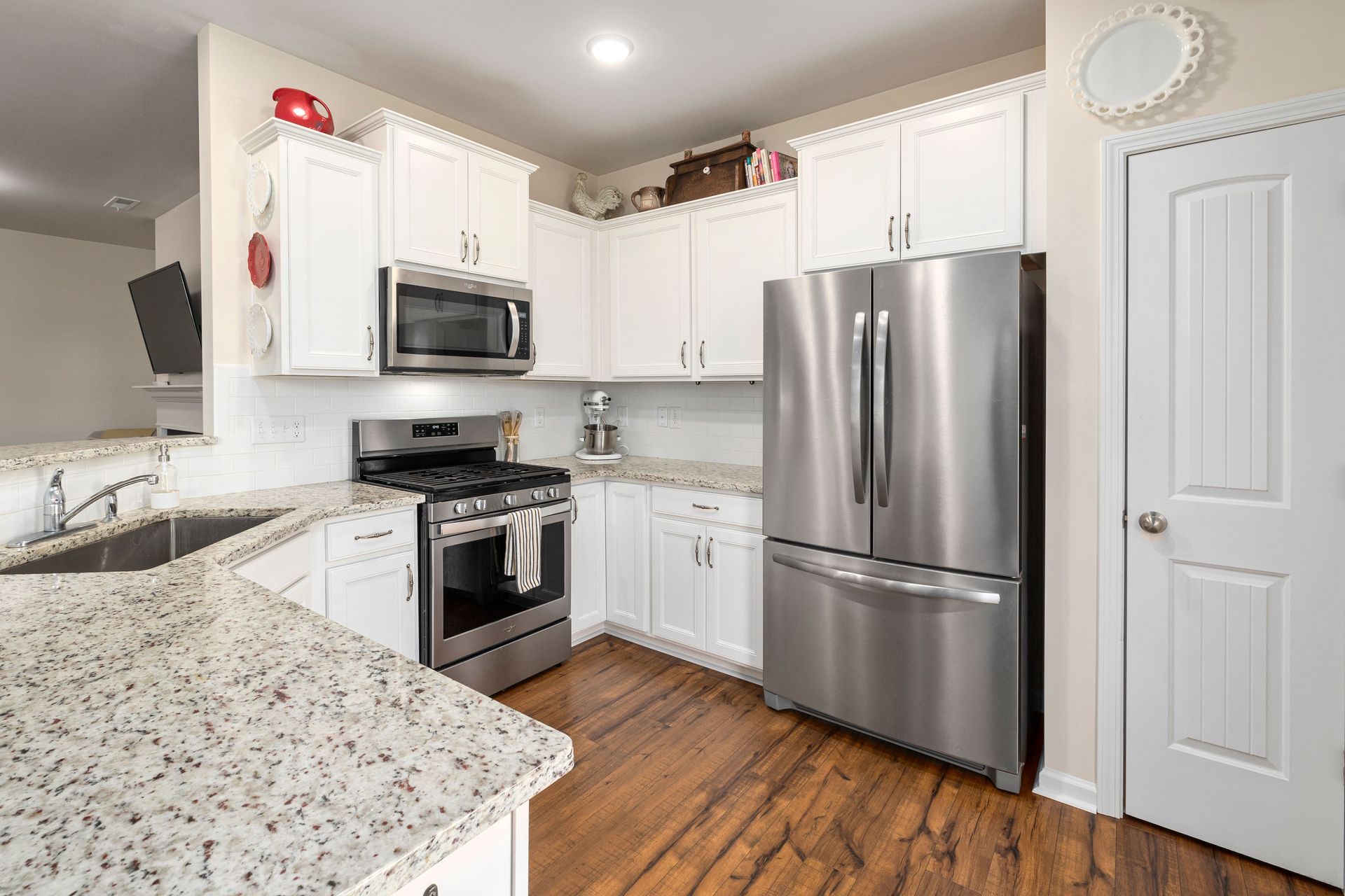 Bright modern kitchen with white cabinets, stainless steel fridge, and speckled granite countertops.
