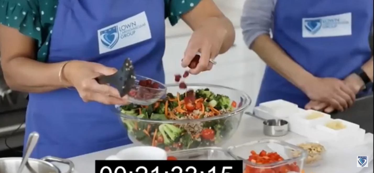 Person adding dried cranberries to a salad in a glass bowl.