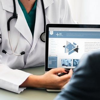 Doctor in a white coat points to a medical website on a laptop screen, consulting with a patient.