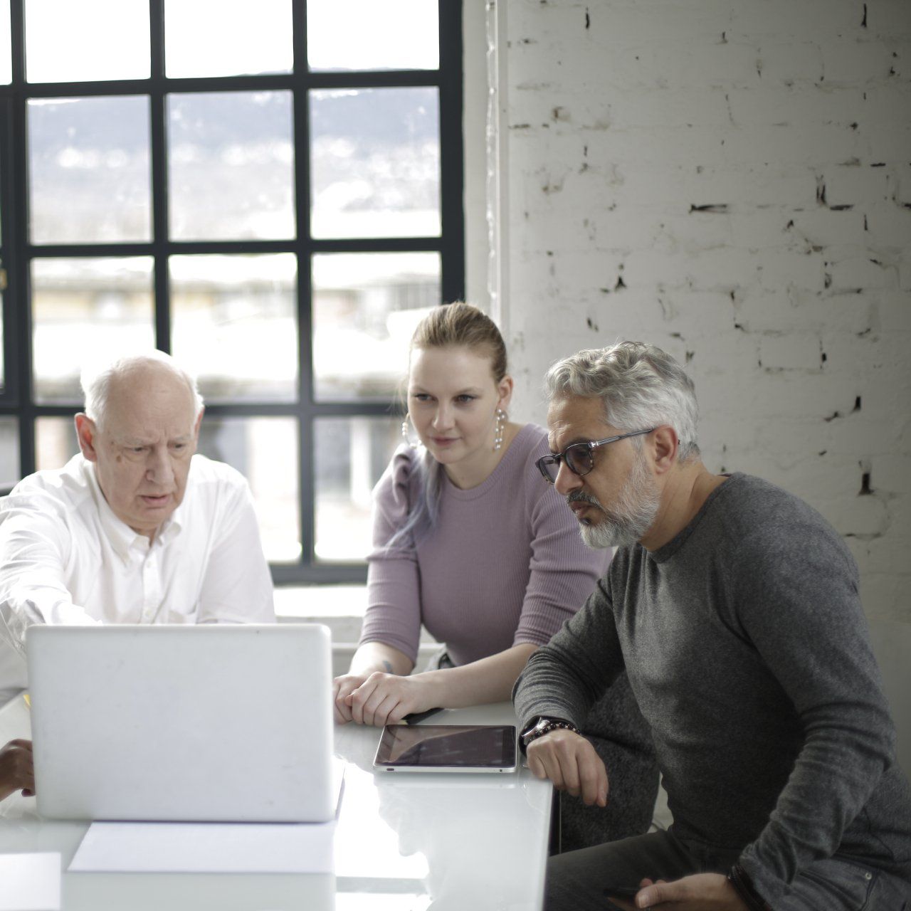 Three people looking at a laptop. Two men and a woman seated in a room with a large window.