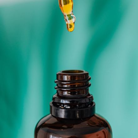 Dropper with oil above a brown bottle against a teal background.