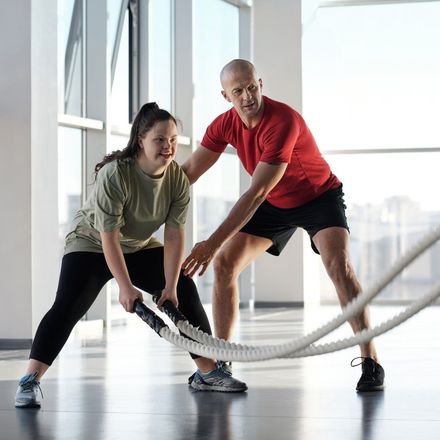 Woman with Down syndrome working out with a trainer using battle ropes in a gym.