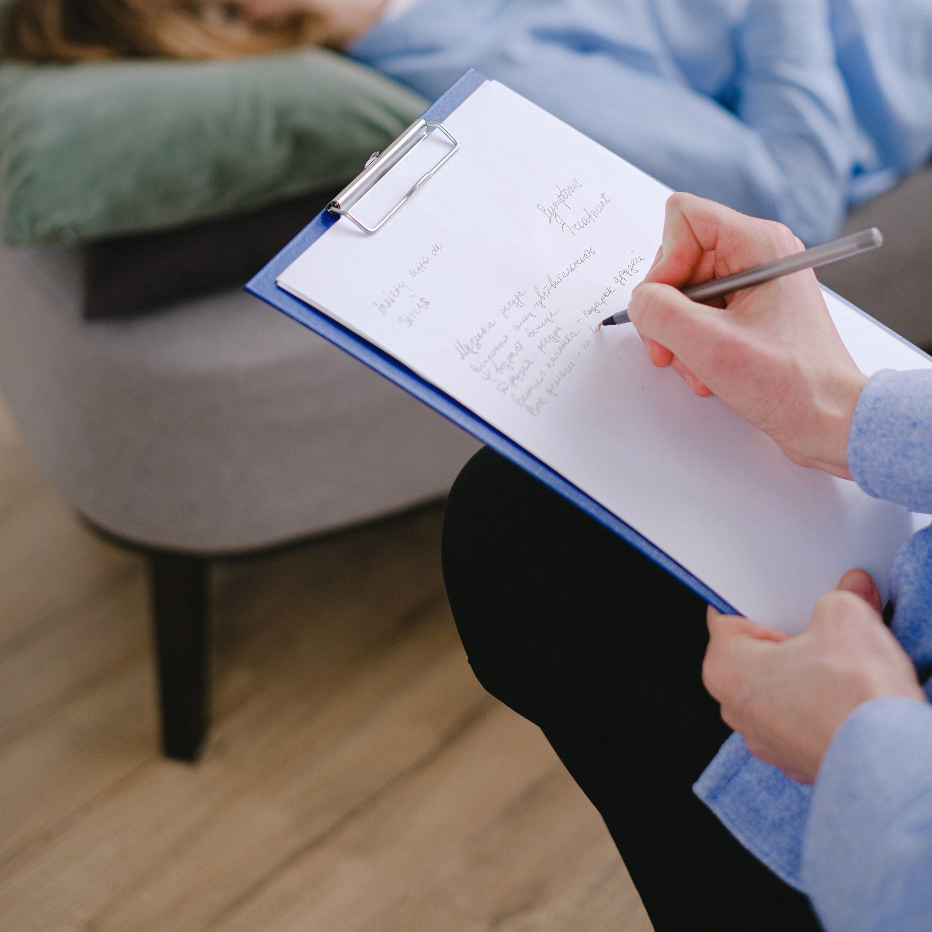 Therapist takes notes on a clipboard while patient reclines on a couch during session.