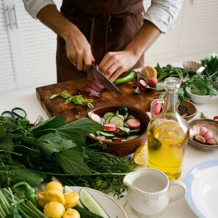 Person chopping vegetables on a wooden board in a bright kitchen with various ingredients.