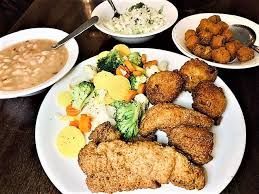 Plated fried fish, rice, veggies, and sides of beans, coleslaw, and fried plantains on a table