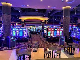 Colorful casino floor with rows of glowing slot machines and lounge seating under purple lighting