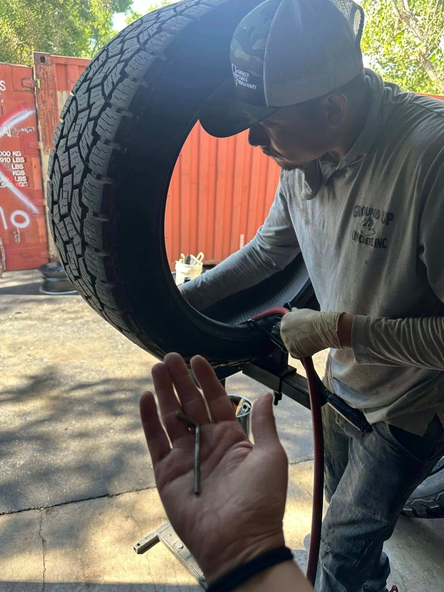 A man is holding a screw in his hand while working on a tire.