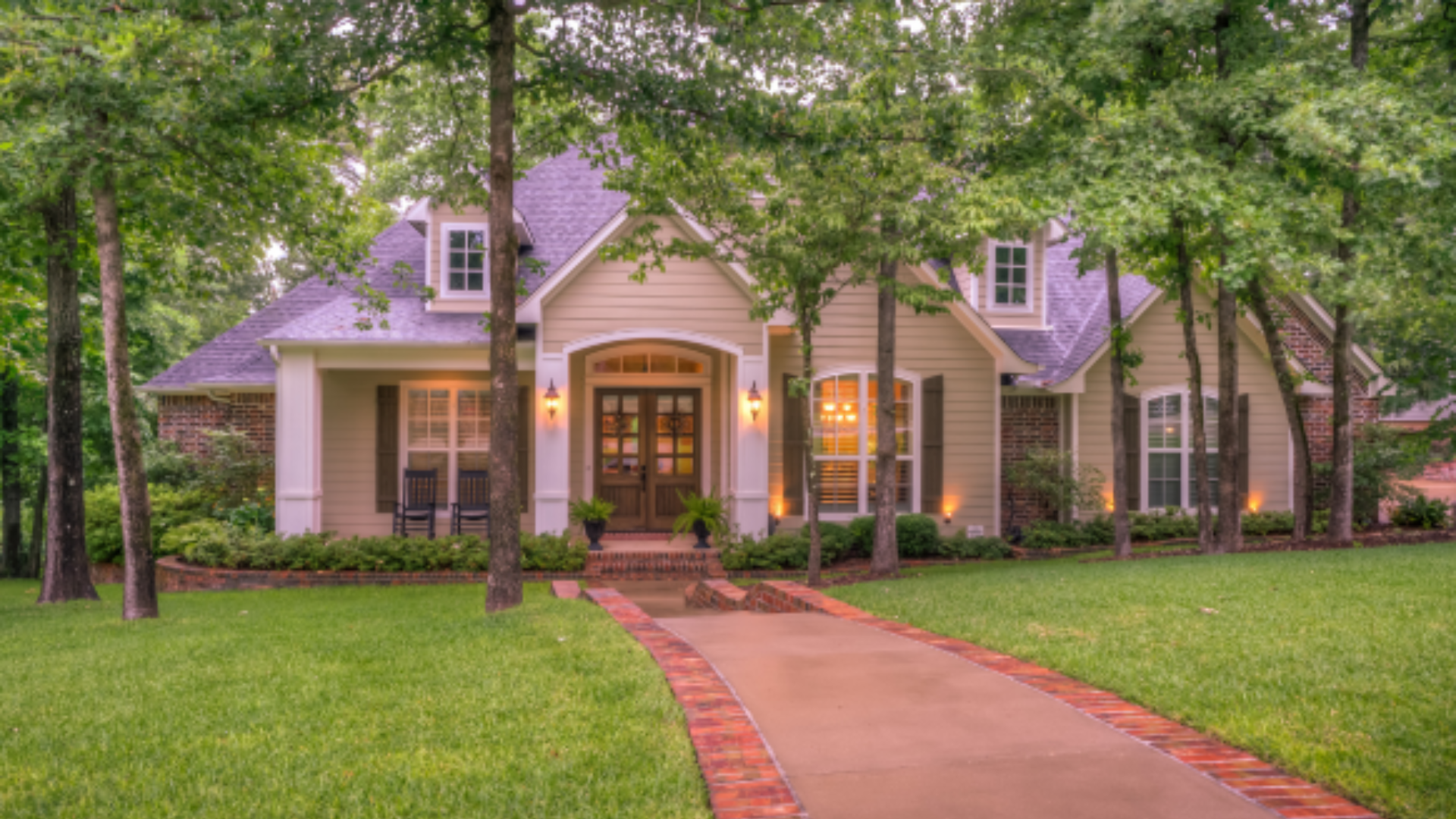 A large house with a brick driveway leading to it is surrounded by trees.
