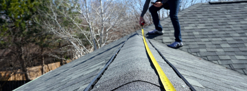 A man is measuring a roof with a tape measure.