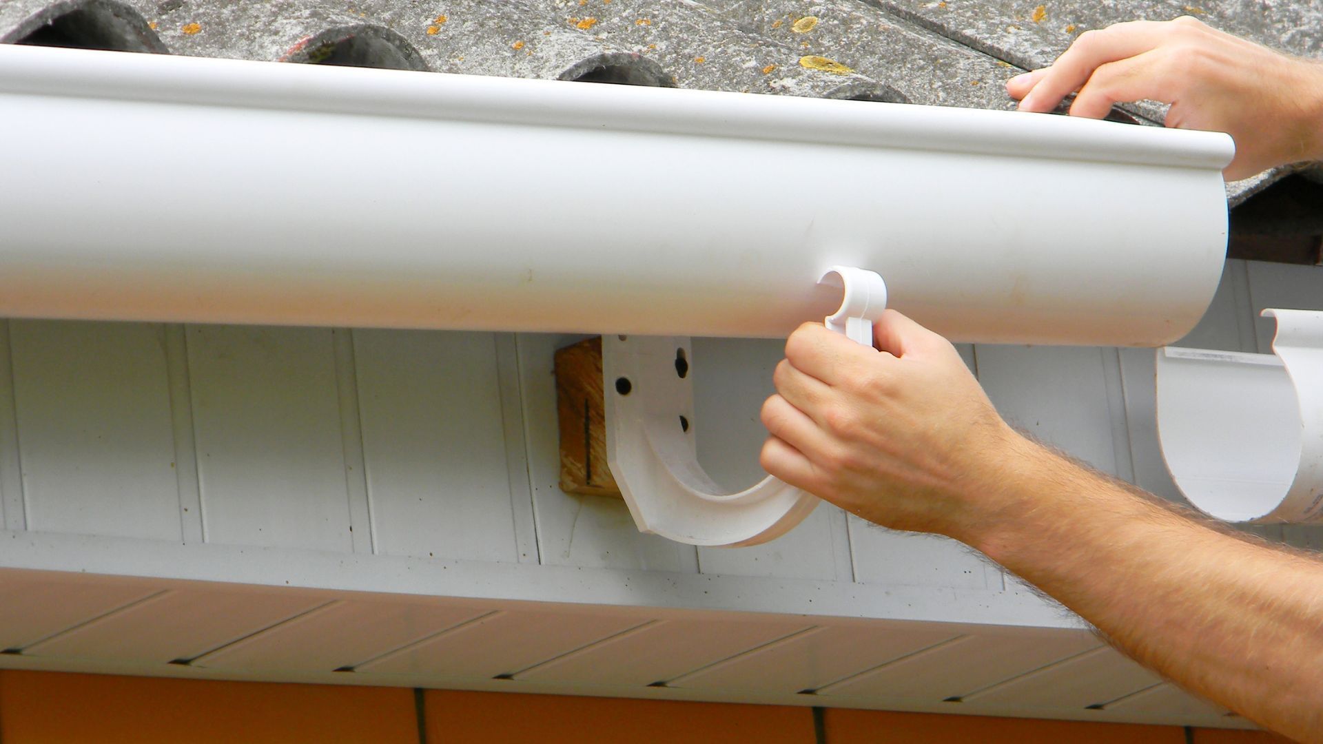 A person is installing a white gutter on a roof.