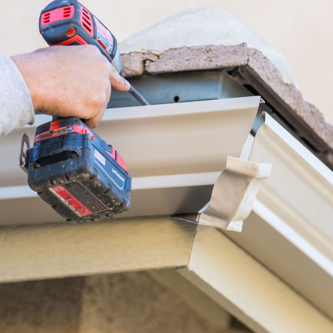 A person is working on a gutter with a cordless drill