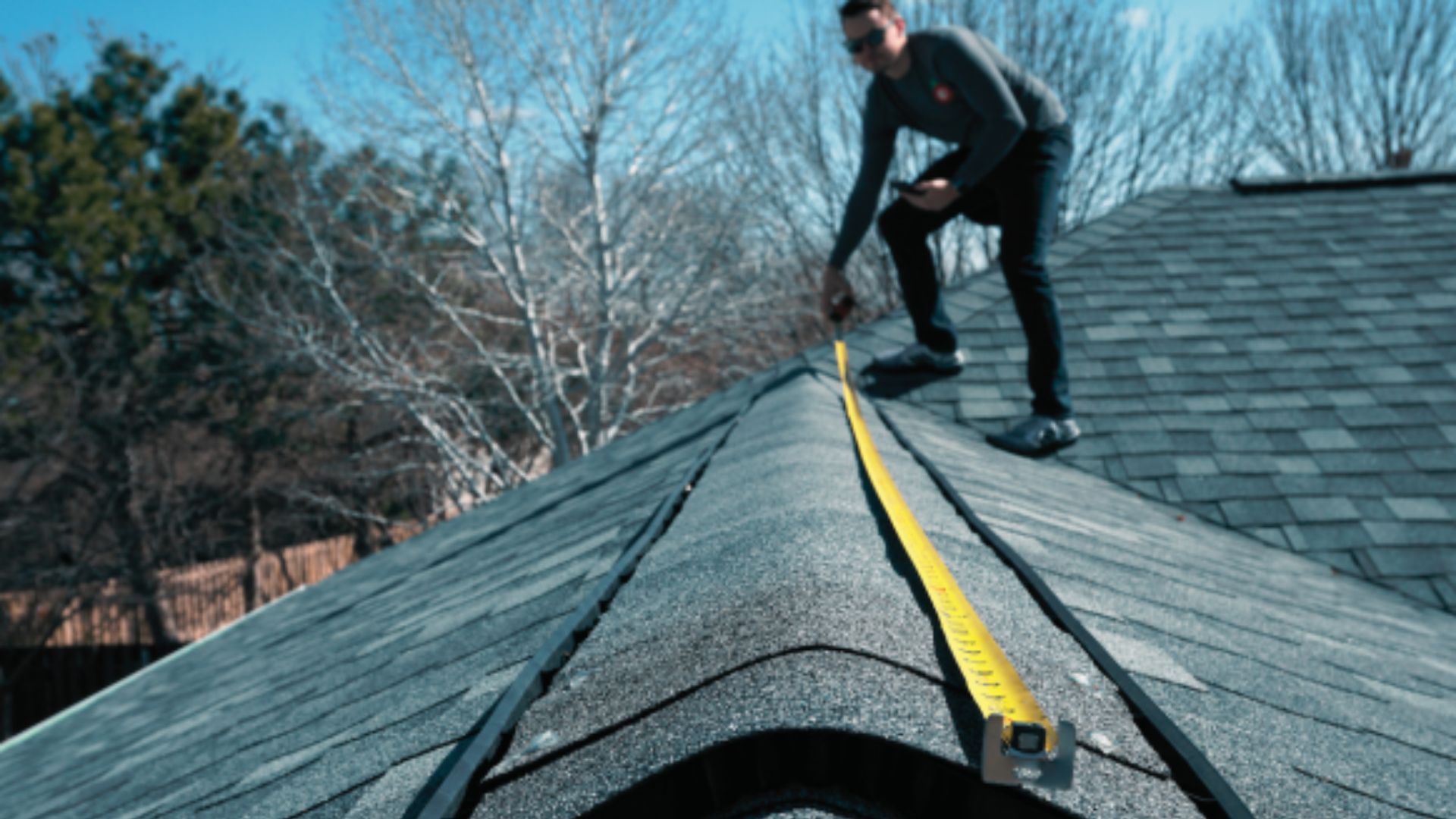 A man is measuring a roof with a tape measure.