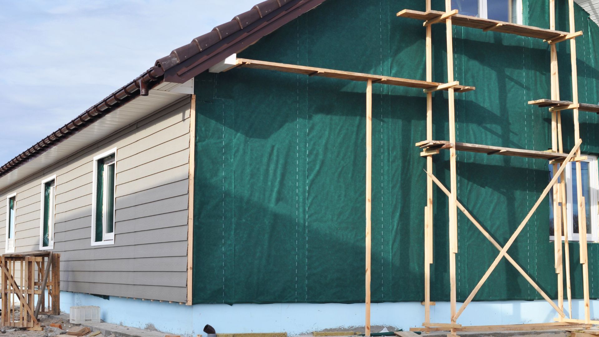 A house is being built with green siding and scaffolding.