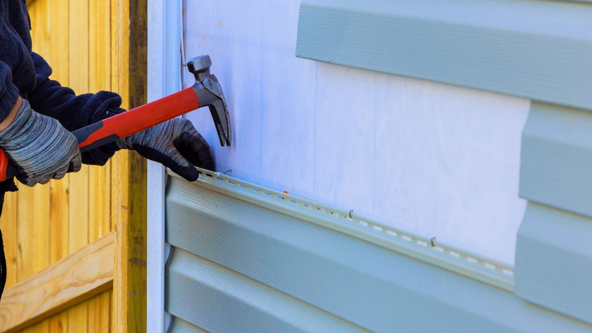 A man is installing siding on a house with a hammer.