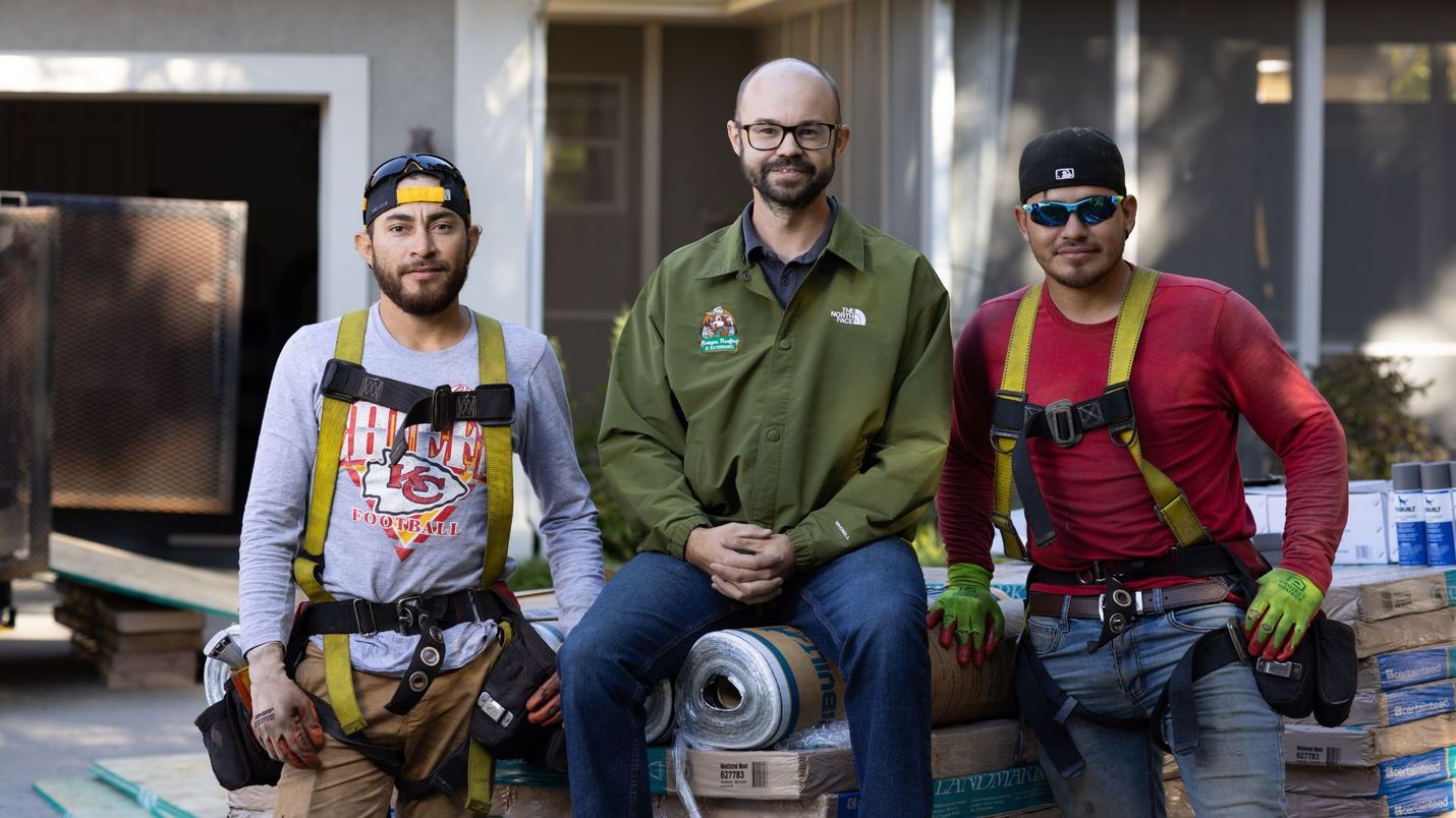 Three construction workers are posing for a picture in front of a house.