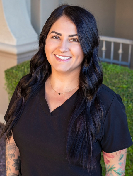 A woman in a black scrub top is smiling and standing in front of a building.