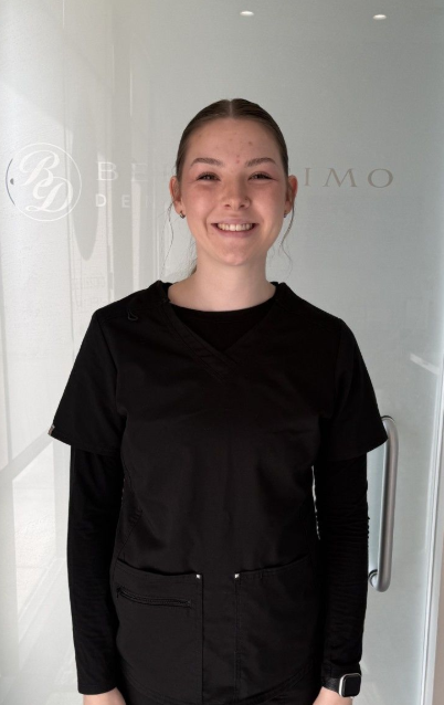 Person standing indoors in front of a frosted glass door, wearing black clothing and smiling.