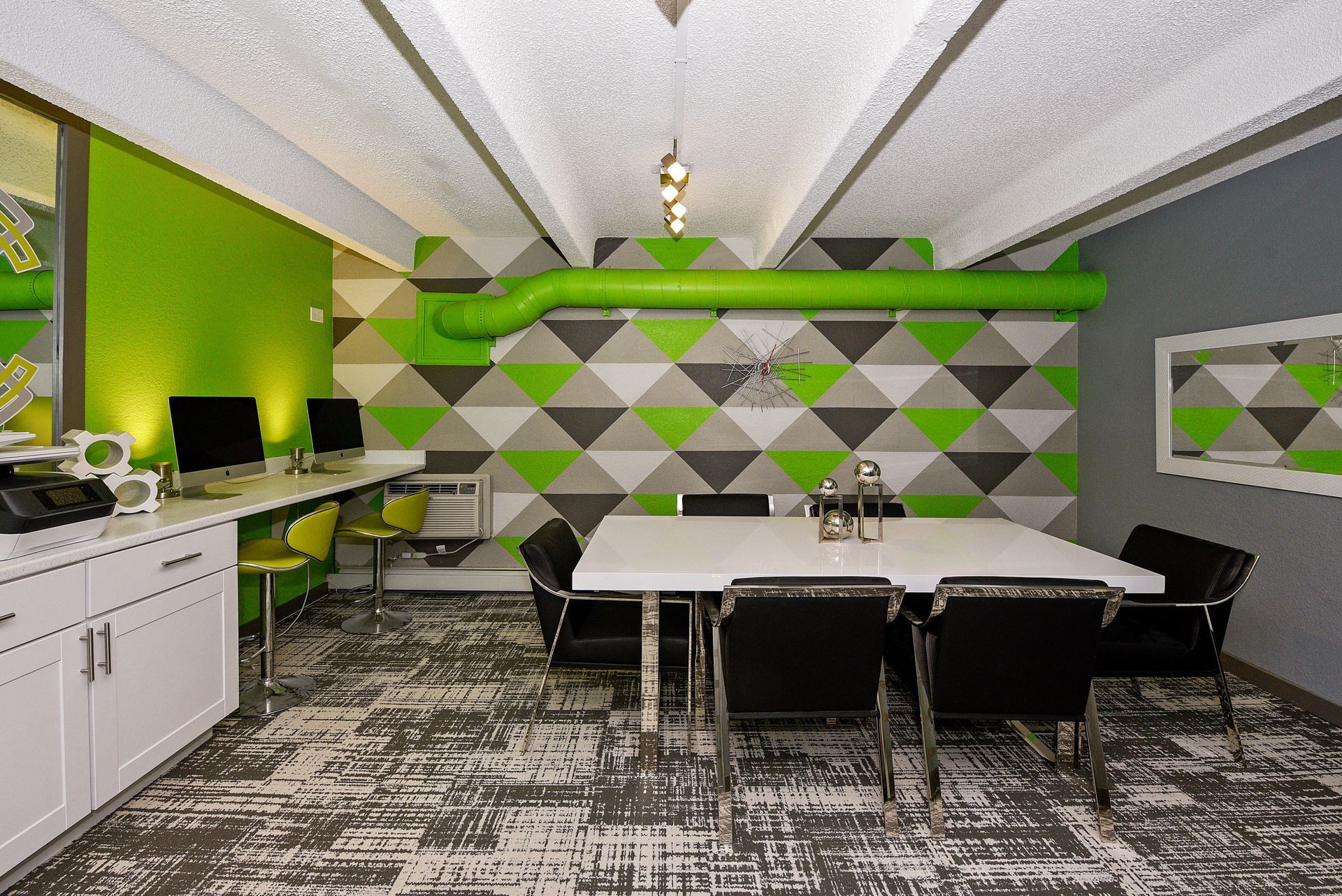 Modern office break room with green accents, white table and chairs, kitchenette, and geometric wall art.
