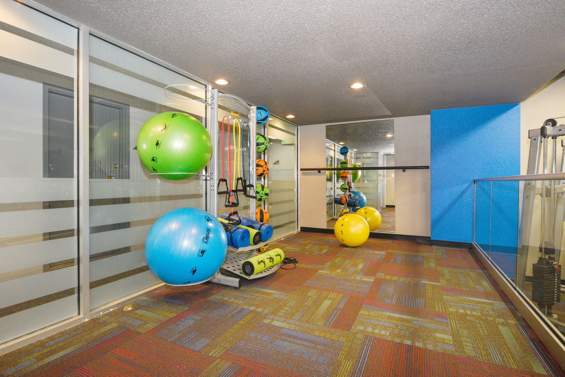 Bright playroom with colorful exercise balls, shelves, and a blue wall mirrored on the right