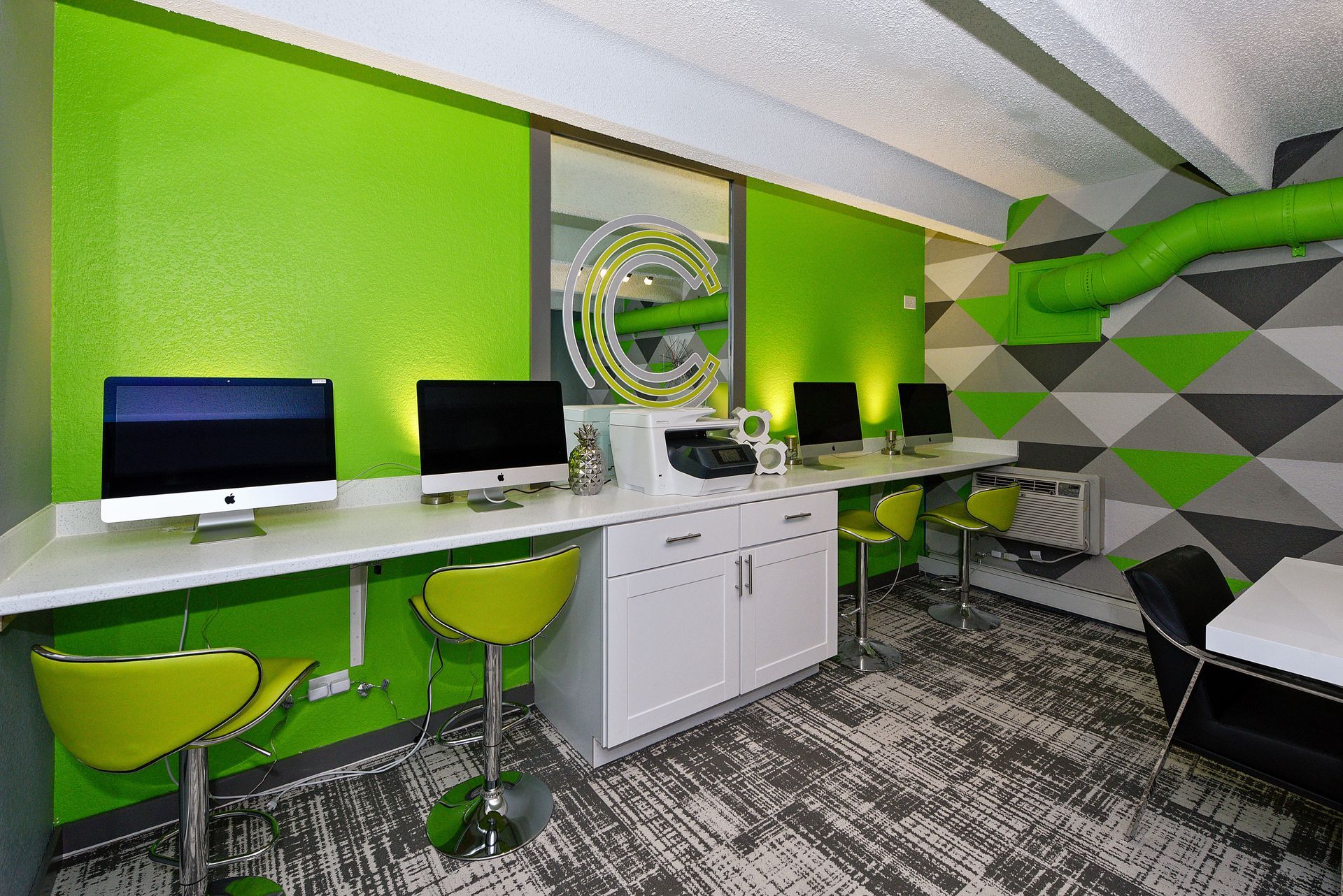 Bright green modern office with two computers, stools, and geometric gray wall accents